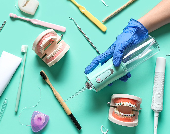 Hand holding a dental water flosser above dental models and hygiene tools, emphasizing oral care after root canal treatment at Linrose Dental.