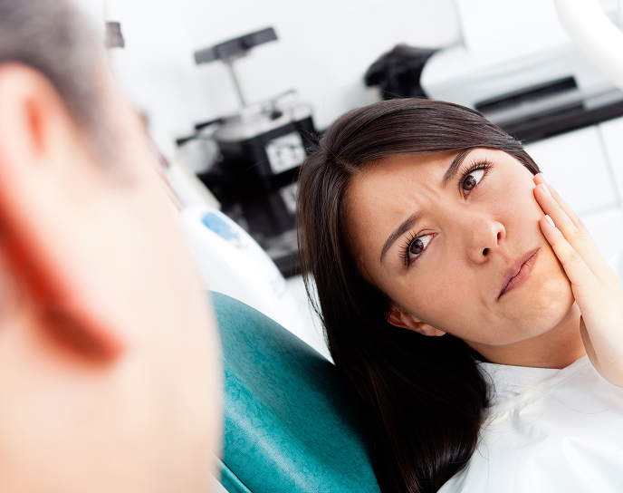 Patient experiencing tooth pain in dental chair, indicating need for root canal therapy, with dental equipment visible in background.
